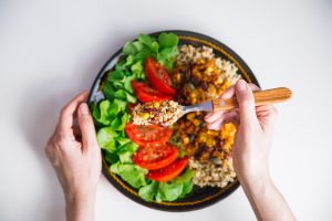 Top view of Female hands at dinner table holding fork above plate with quinoa, red beans, corn, tomato and green salad